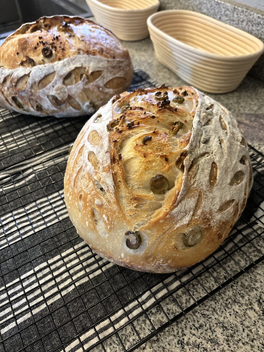 Olive and garlic sourdough loaves with beautiful scoring, bannetons visible in background